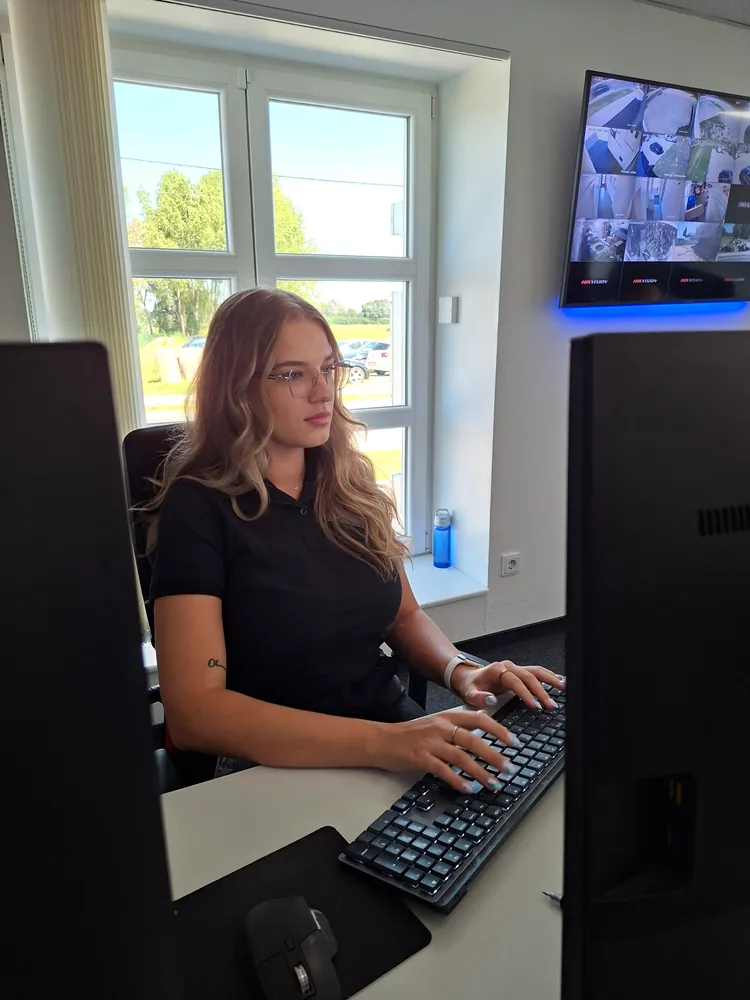 Djelatnica Zaštite Jukić za radnim stolom, uz nju zidni monitor s podijeljenim prikazom kamera videonadzora