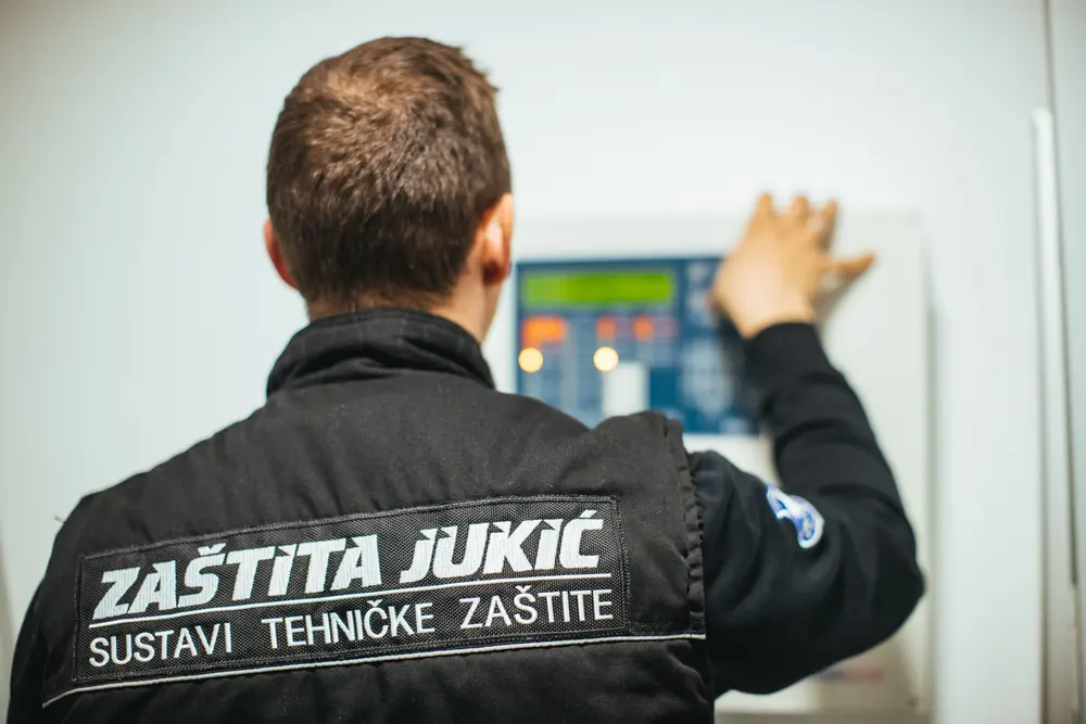 Serviser Zaštite Jukić u brendiranoj radnoj jakni provjerava centralu sustava tehničke zaštite na zidu
