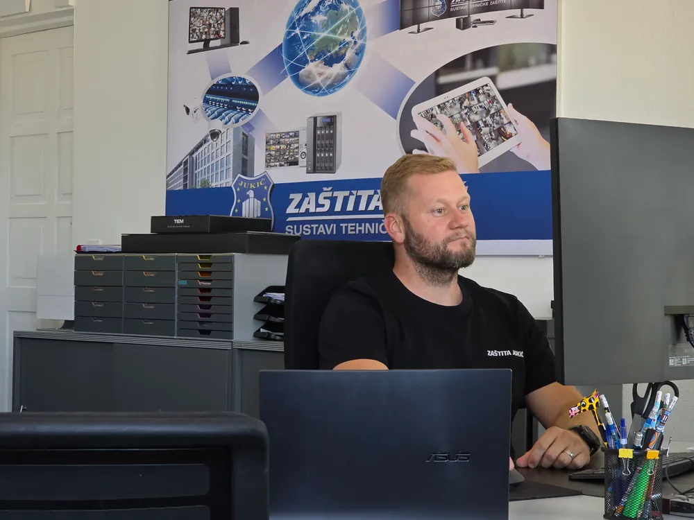 Djelatnik Zaštite Jukić radi za prijenosnim računalom ispred plakata tvrtke u uredu
